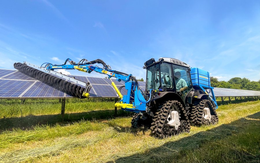 SunBrush® TrackFlex montado en un tractor, limpiando con el brazo extendido una hilera de módulos en un parque solar