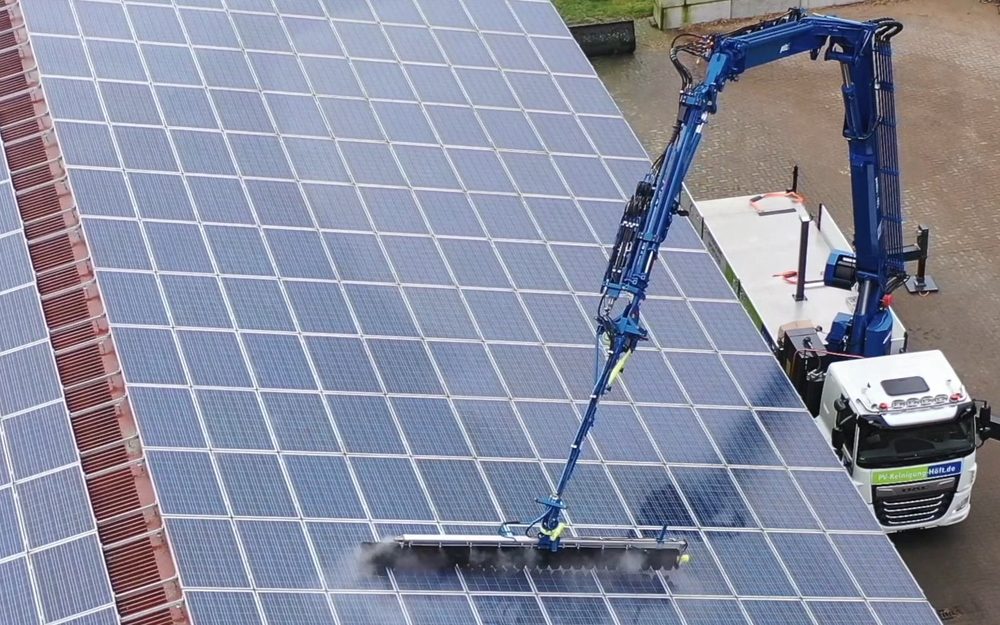 SunBrush® Crane montado en la grúa de un camión, limpiando una instalación fotovoltaica sobre un techo